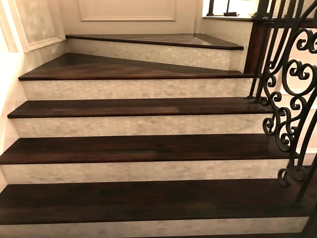 Close crop of dark wood stair treads with pearl risers and an ornate wrought-iron railing.